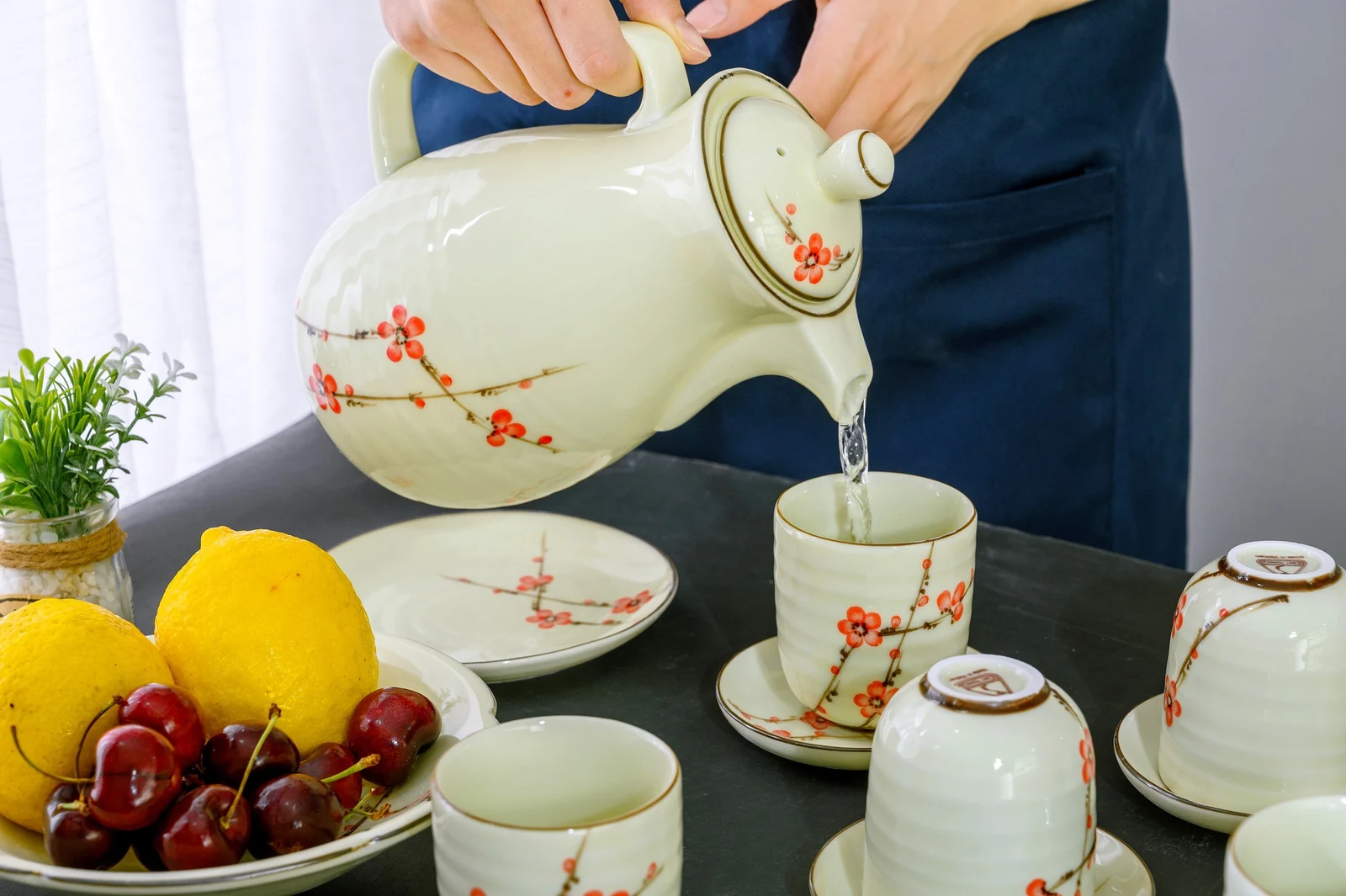 Một người giữ nắp và rót nước từ ấm hoa đỏ vào cốc cùng bộ