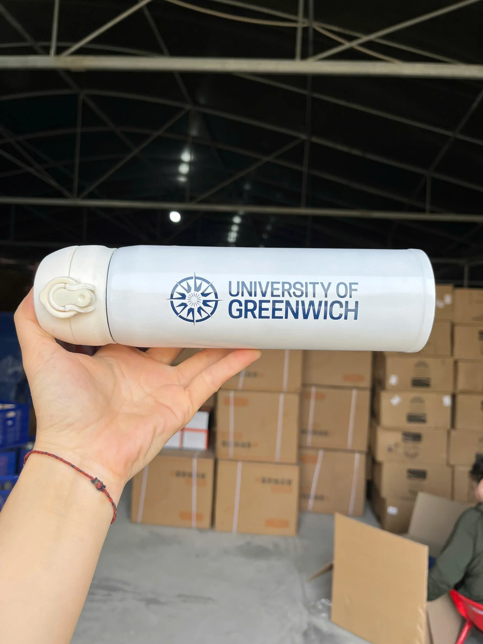 Tay cầm bình trắng UNIVERSITY OF GREENWICH trước các thùng carton