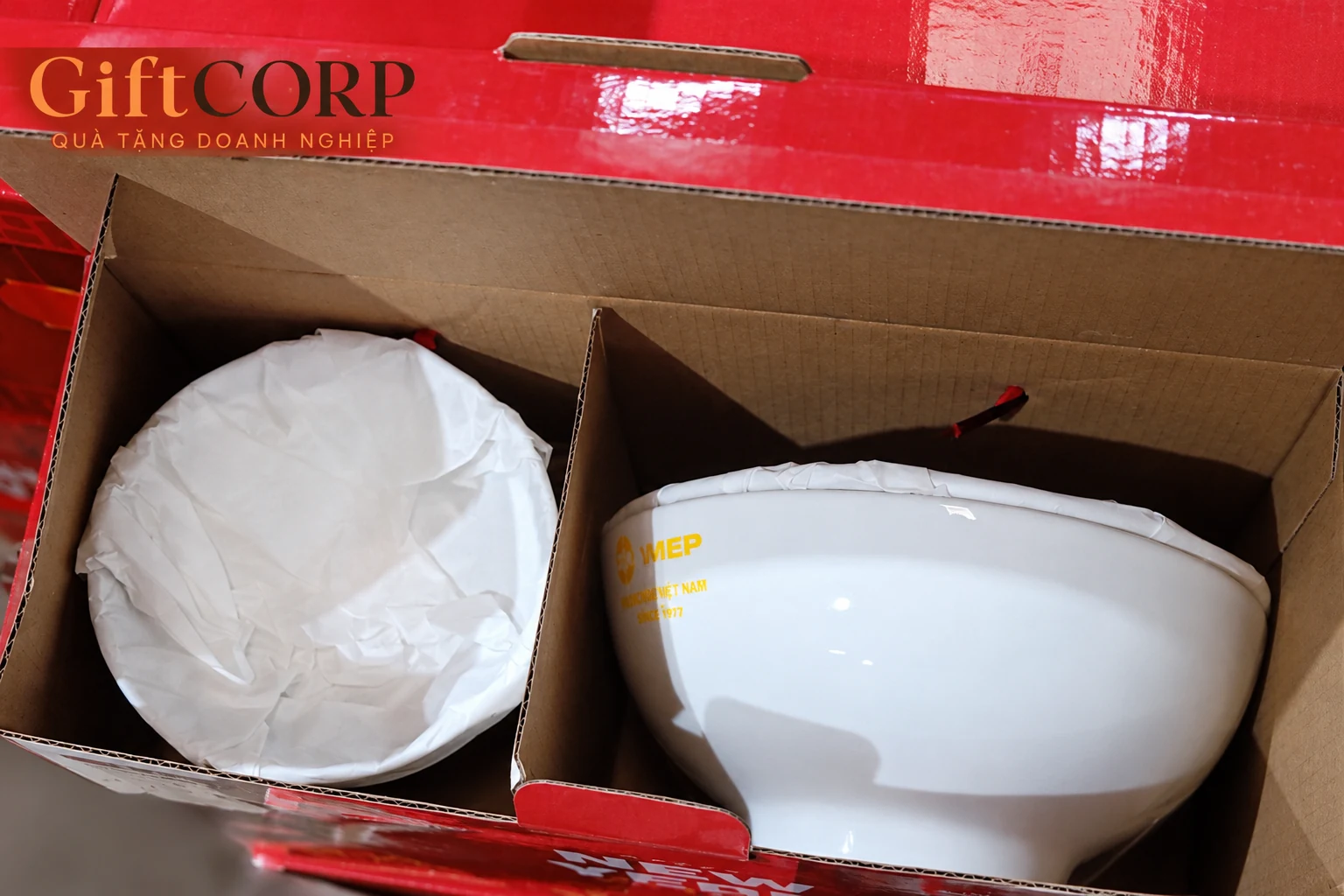 Góc cận vách carton giữa món đồ sứ bọc giấy và bát trắng