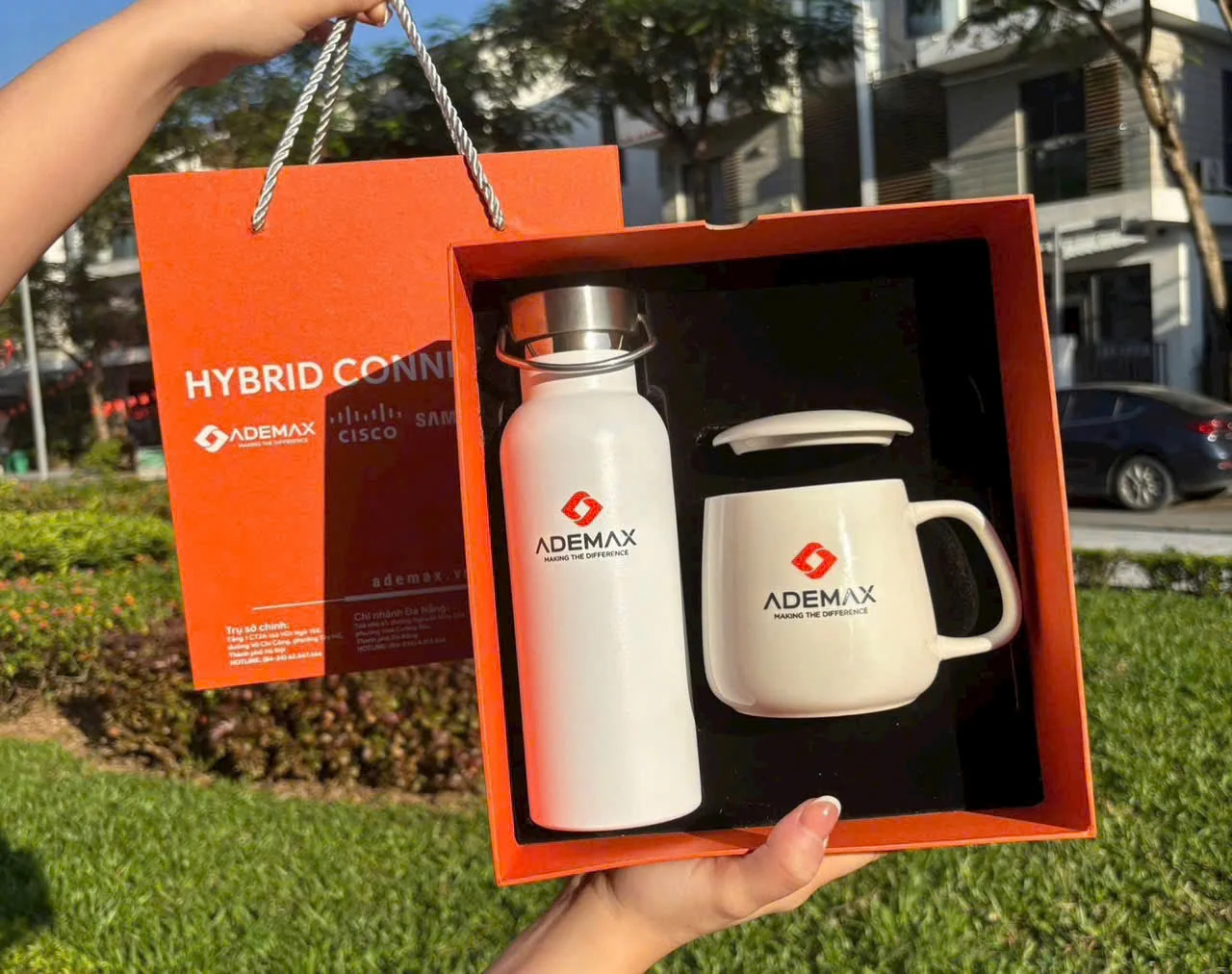 Tay cầm hộp cam có bình trắng, cốc trắng có nắp và túi cam mang nhận diện ADEMAX
