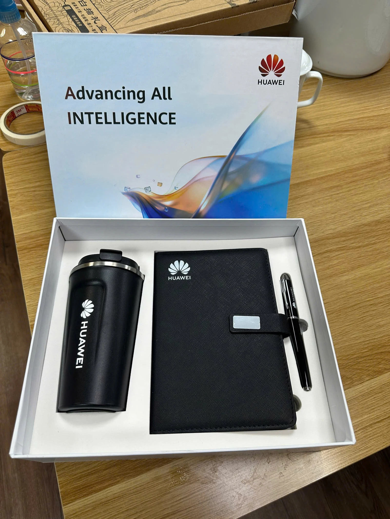 Ly đen, sổ đen, bút và hộp có nhận diện Huawei trên bàn gỗ