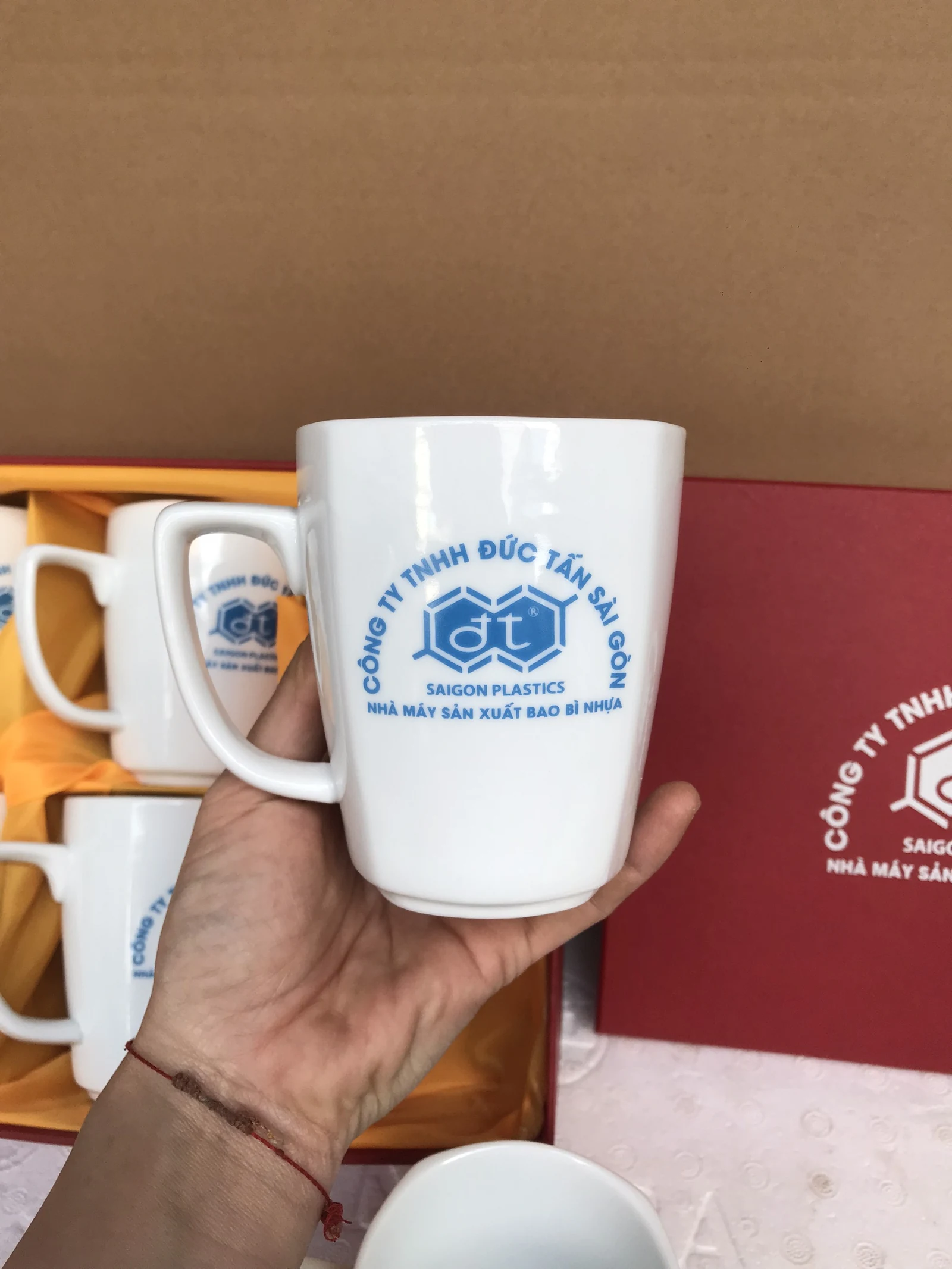 Tay cầm cốc trắng có chữ vòng cung, biểu tượng và hai dòng xanh nhỏ trên thân