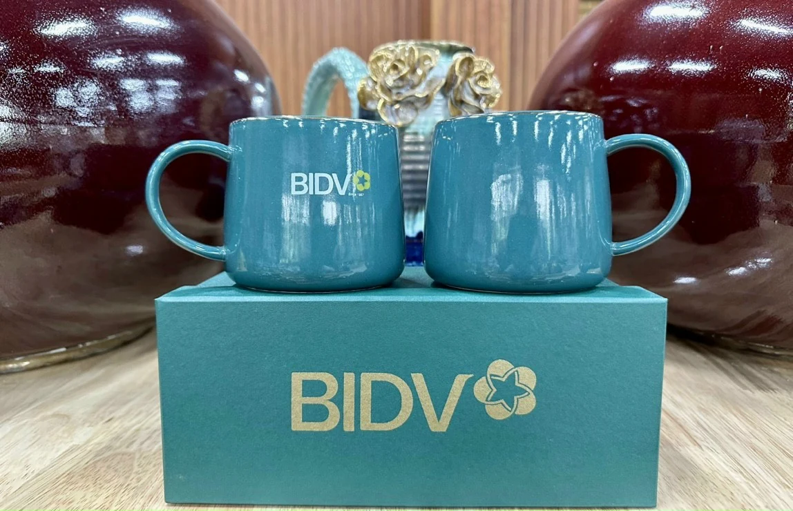 Hai cốc men xanh quai tròn trên hộp, một mặt có logo BIDV trắng vàng và một mặt trống
