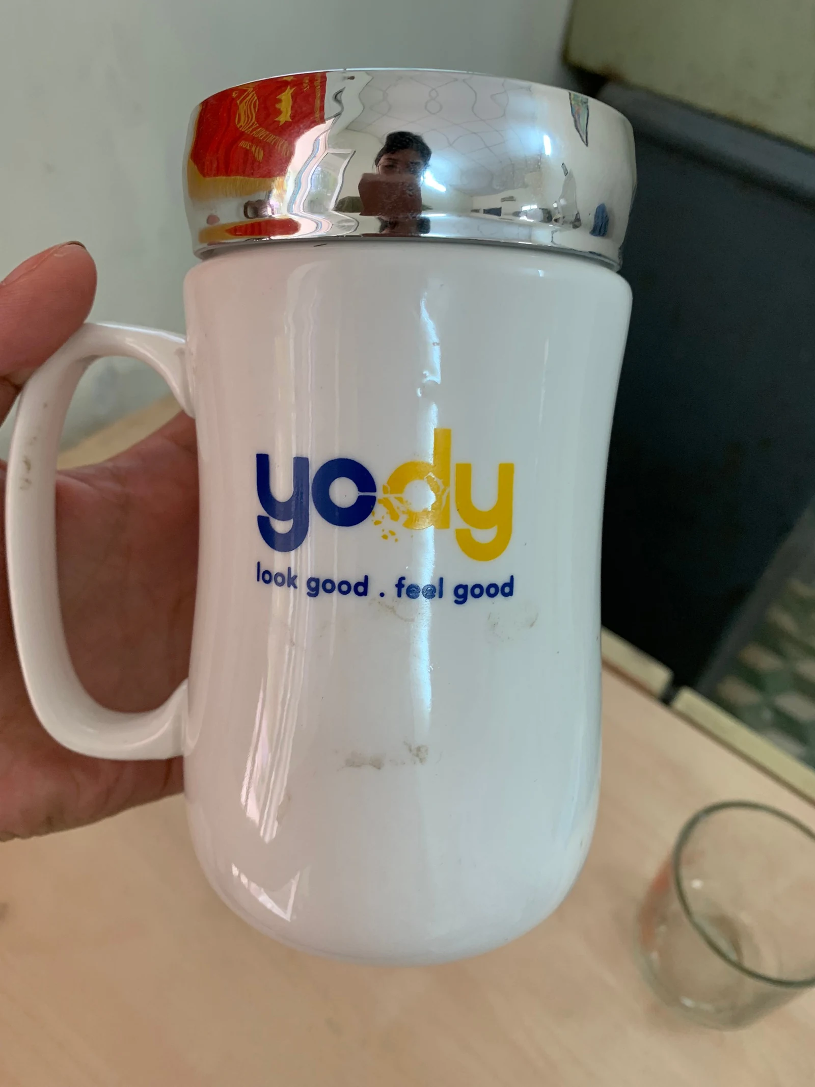 Cốc trắng có logo xanh vàng và dòng chữ nhỏ bên dưới, được cầm trên tay