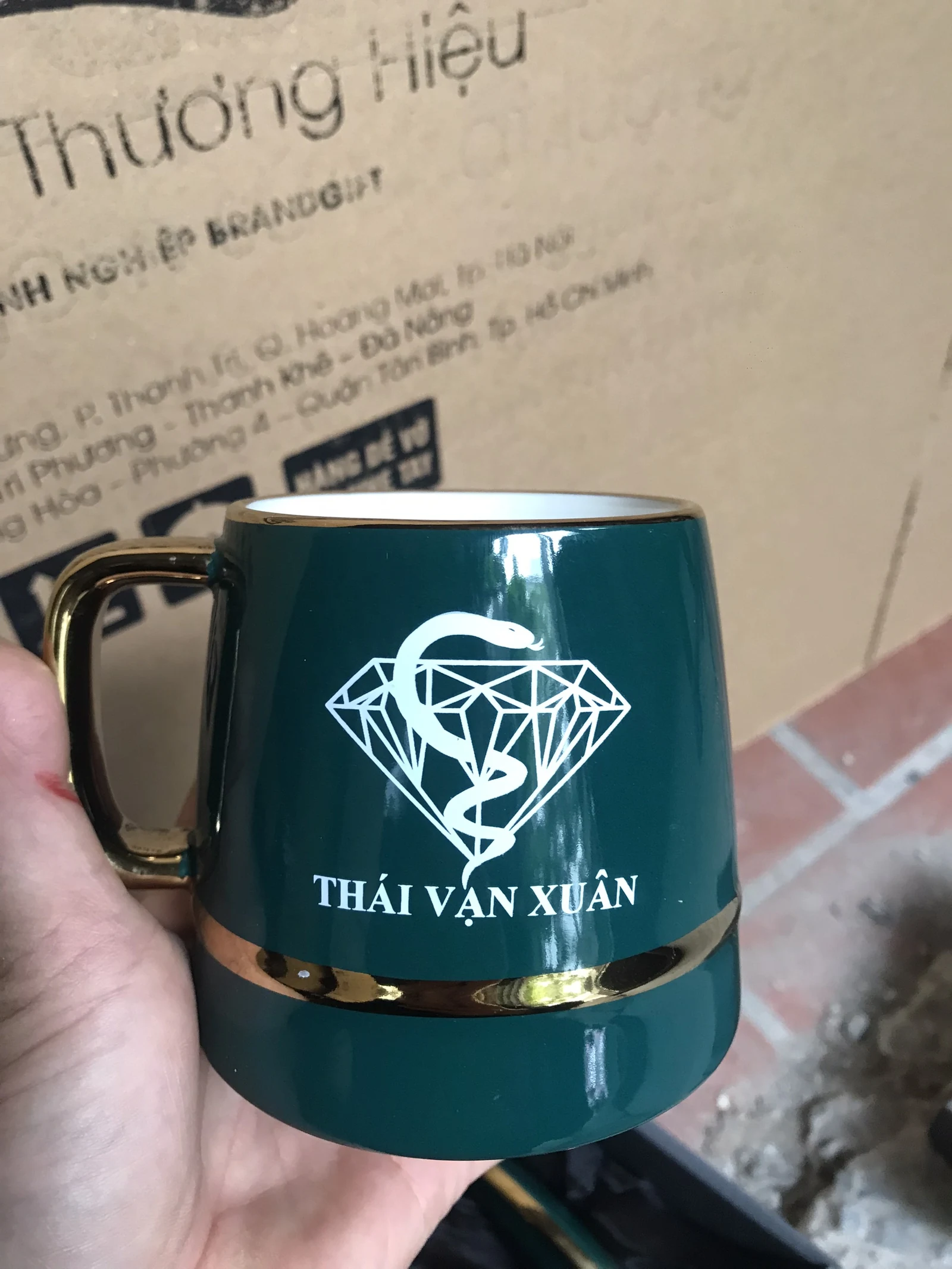 Cốc xanh có viền quai ánh kim, biểu tượng nét trắng và dòng Thái Vạn Xuân