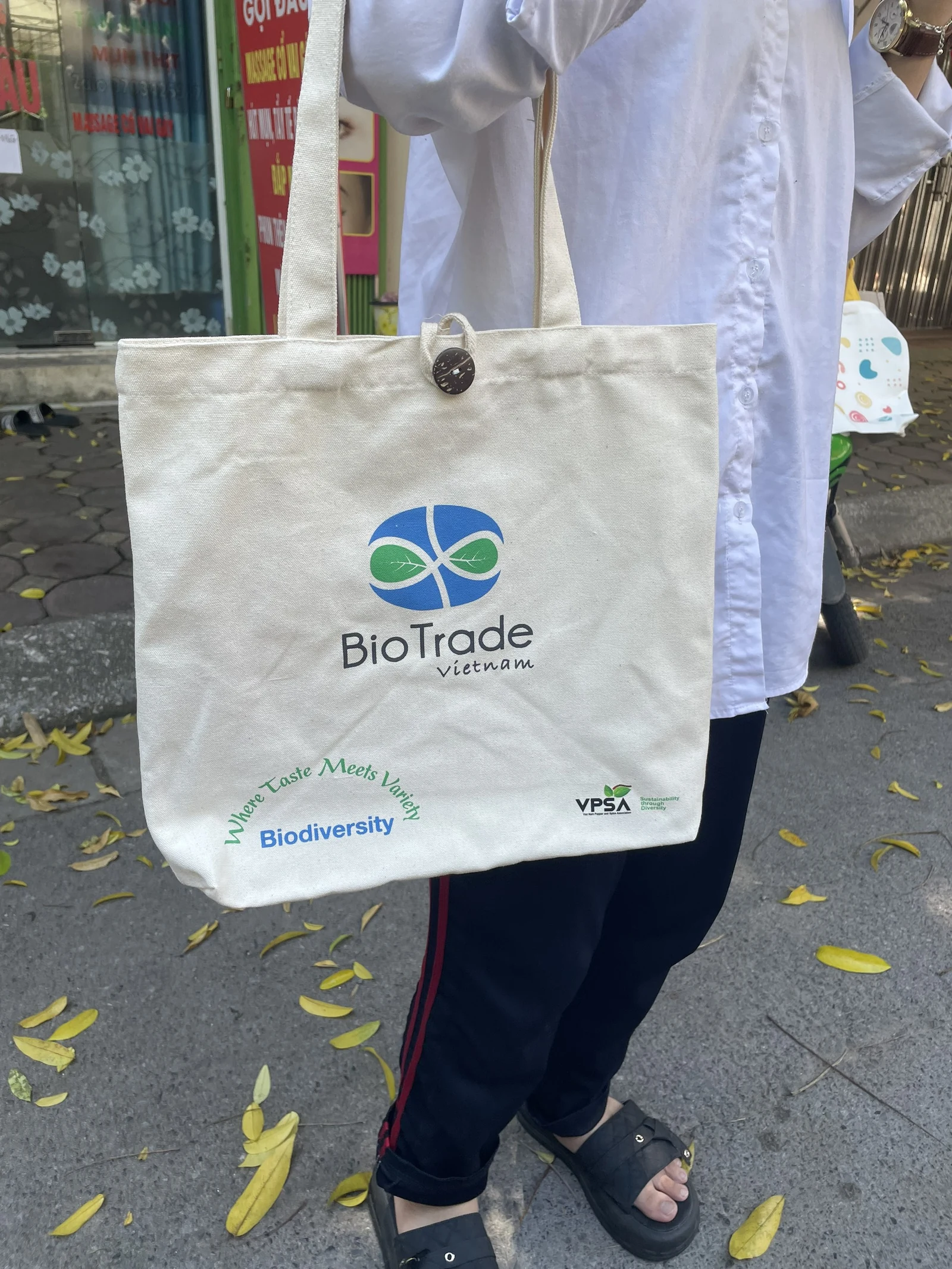 Người mặc áo trắng đeo túi kem có logo BioTrade Vietnam xanh và chữ ở phần dưới