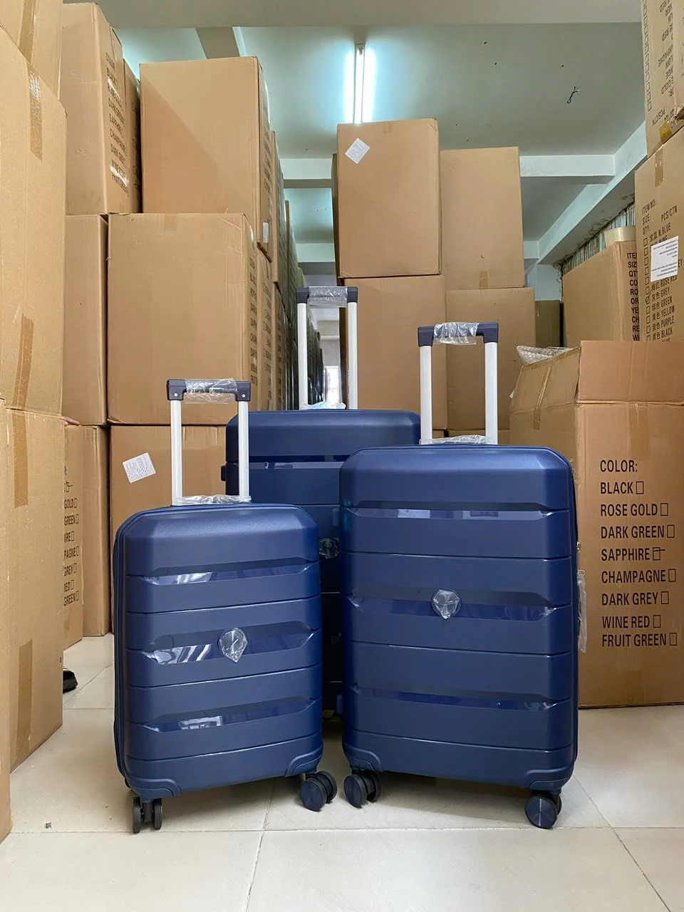 Ba vali xanh có kích cỡ khác nhau đứng trước các thùng carton