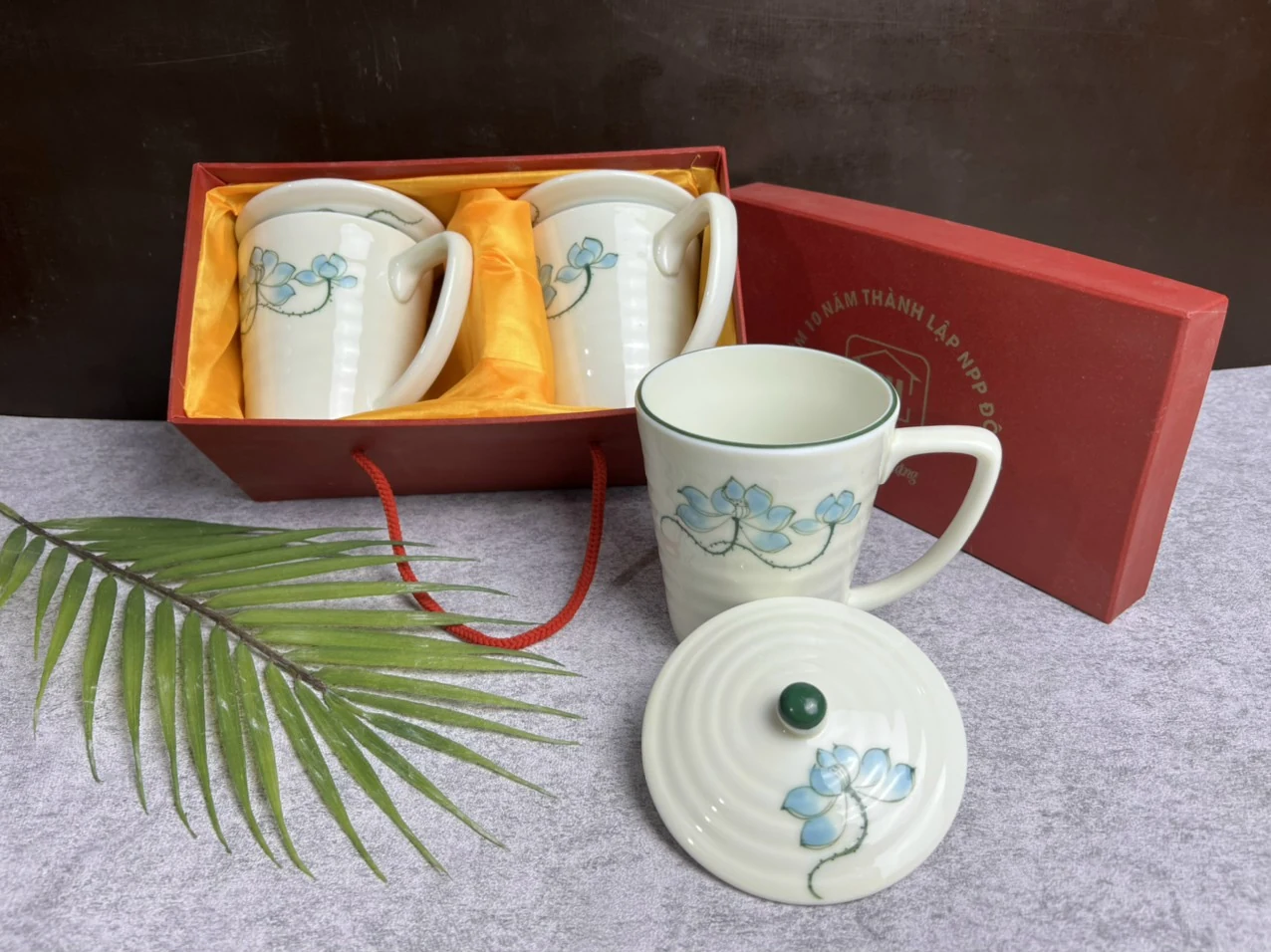 Cốc trắng có họa tiết hoa xanh, nắp rời phía trước và hộp đỏ bên cạnh