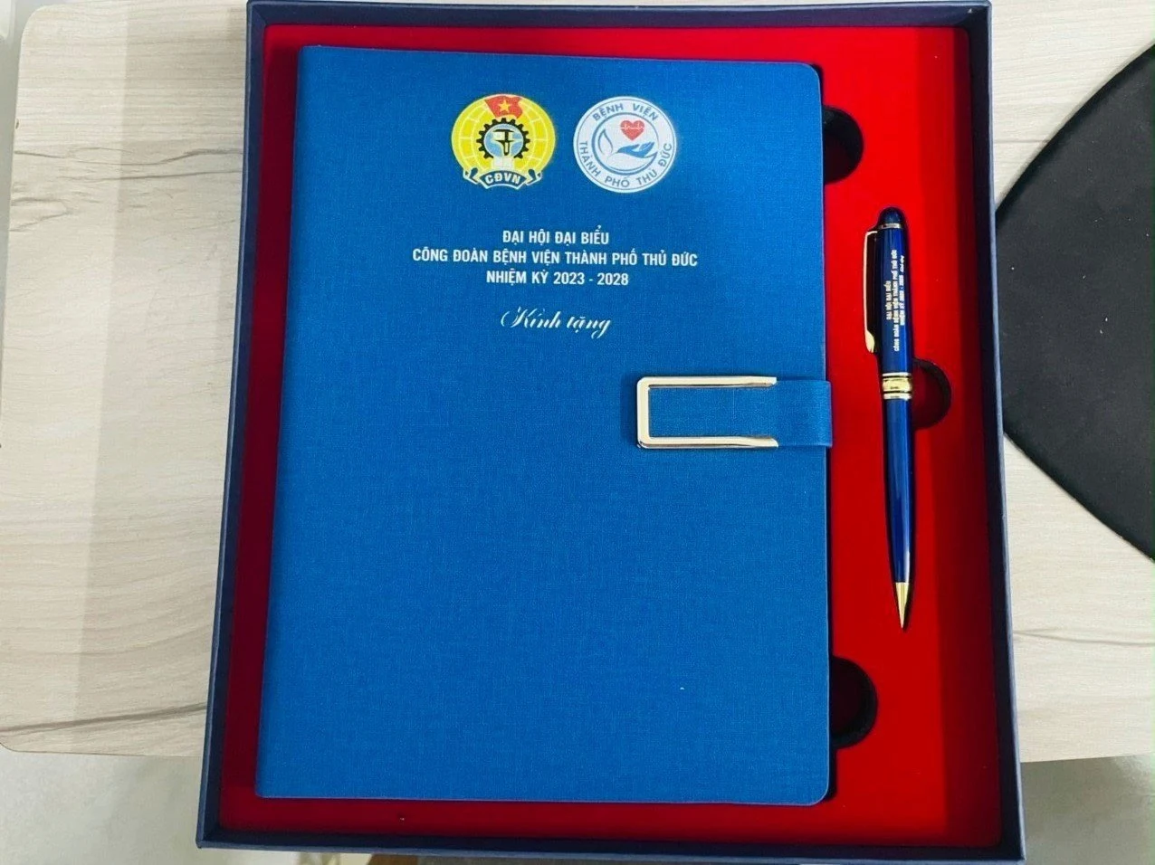 Hộp sổ xanh và bút trên khay đỏ in nội dung Đại hội công đoàn Bệnh viện thành phố Thủ Đức