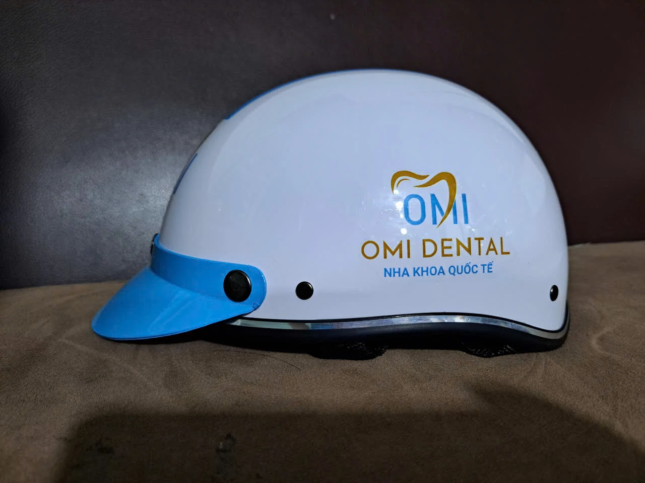 Mặt bên mũ trắng và vành xanh có logo và dòng chữ OMI Dental