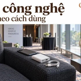 Cảnh dựng góc nghỉ hội nghị có điện thoại, sạc dự phòng và dây rời trên ghế, quạt cầm tay bên cửa kính, chữ Quà công nghệ Chọn theo cách dùng cùng logo GiftCorp